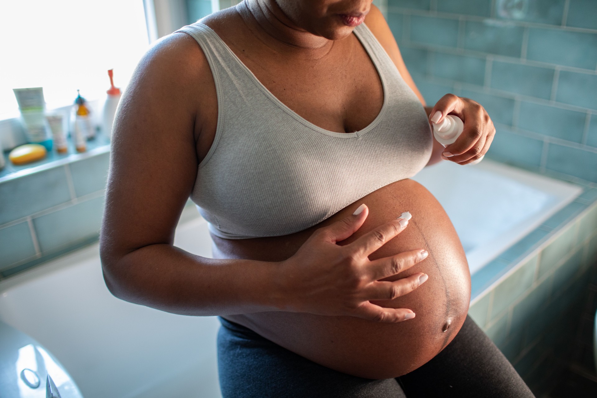 Young pregnant Hispanic woman using a spray cream on her belly