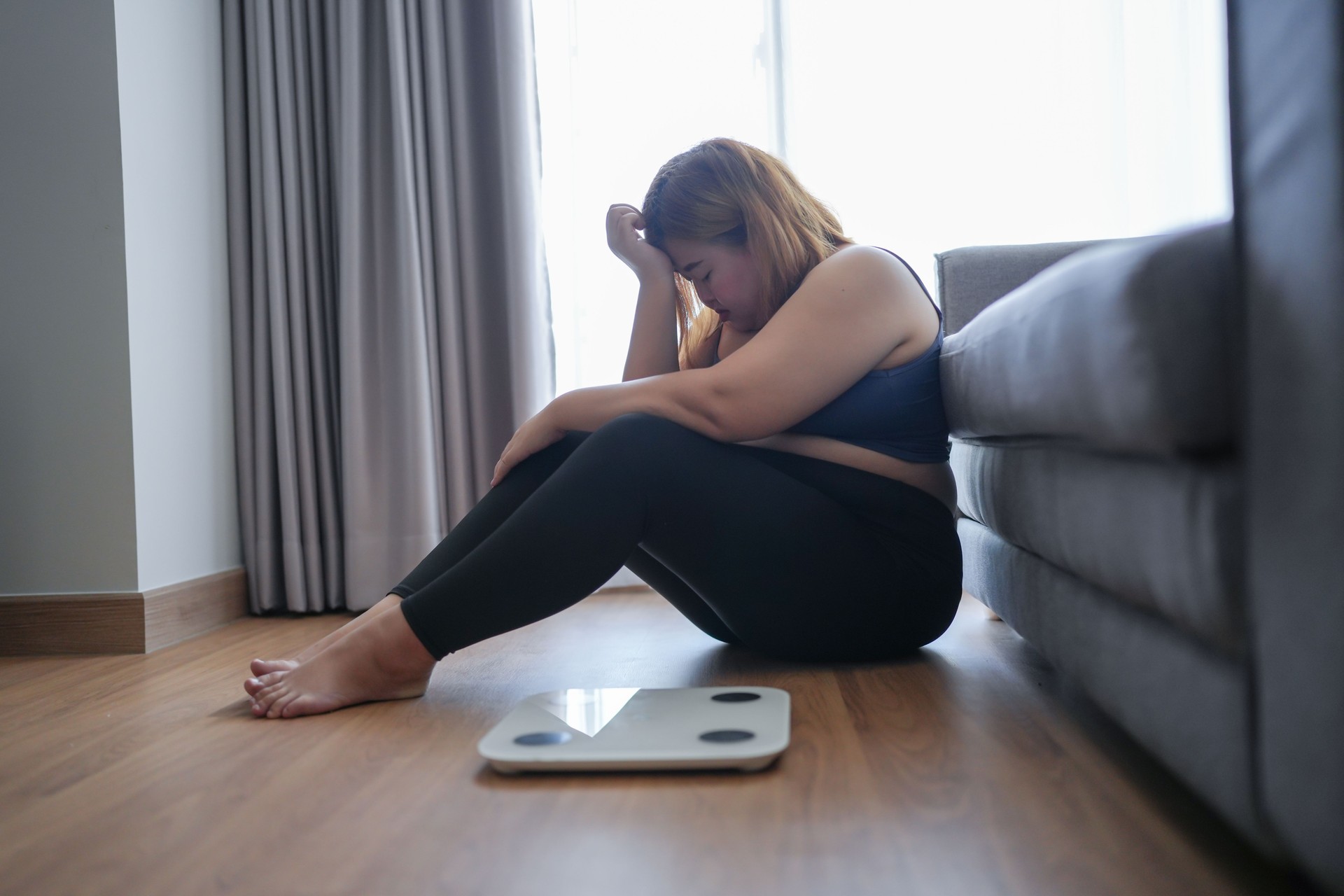 Sad fat woman with fat upset bored of dieting Weight loss failÂ  Fat diet and scale sad Obese asian female on weight scale at home weight control